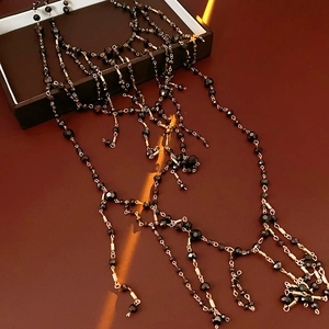 Macro detail of multi-layered tassel necklace with black beads and gold chains on a display box
