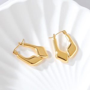 Macro shot of 18K gold irregular geometric hoop earrings on a textured shell tray