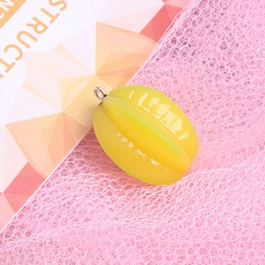 Macro shot of yellow starfruit resin charm with metal ring on pink background