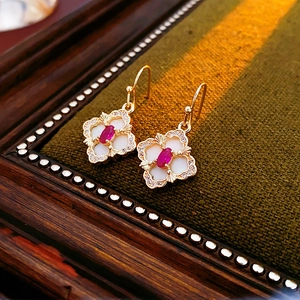 Macro shot of gold four-leaf clover earrings with red gemstone and mother of pearl detail