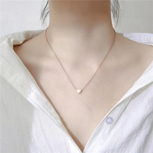 Collier minimaliste avec pendentif cœur en or rose porté avec une chemise blanche