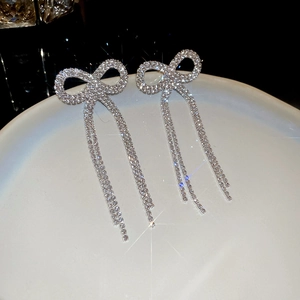 Macro shot of silver bowknot tassel earrings with sparkling rhinestones on a white tray