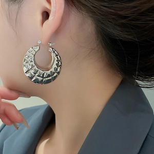 Macro detail of silver hoop earring with irregular wavy texture on a female model