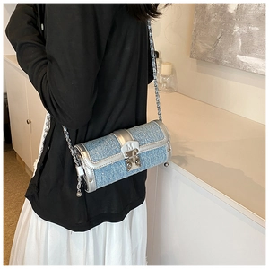 Detail of blue tweed cylinder bag with silver chain strap and metal buckle M on a model