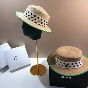 Flat top straw boater hat with green trim and polka dot ribbon shown on a display stand