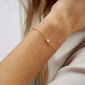 Close-up of a delicate gold chain bracelet with a single round white pearl on wrist