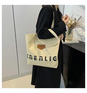 Side view of a creamy canvas tote bag with black lettering and leather patch on model