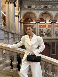 Chic white oversized blazer suit and trousers set styled with a black handbag in an urban setting