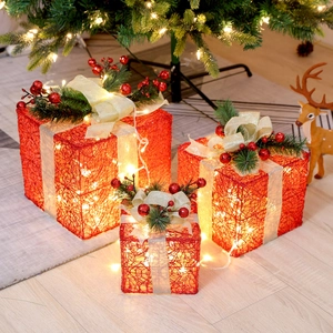 Close-up of three red metal Christmas gift boxes with warm LED lights and golden bows