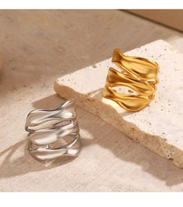 Detailed view of irregular wavy wide band rings in gold and silver on stone props