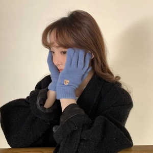 Close-up of blue knitted gloves with cute bear embroidery on soft winter fabric