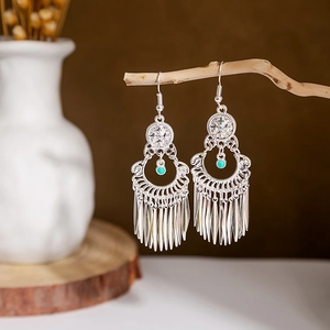 Detail of vintage silver peacock tassel earrings with teal beads on a wooden branch