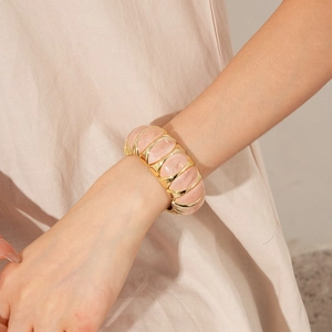 Detail of pink resin and gold metal segmented wide bracelet worn on the wrist