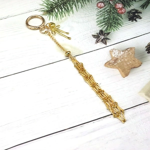 Détail d'un pendentif doré à pompon en maille avec nœud élégant sur fond de bois blanc