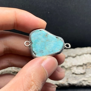 Macro detail of irregular turquoise stone connector with silver metal edge and dual loops