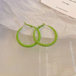 Detail view of neon green geometric hoop earring on textured white paper and vintage card