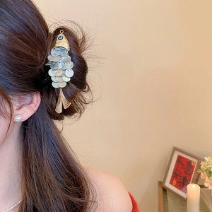 Close-up of a fish-shaped shell hair clip with gold accents on dark brown hair