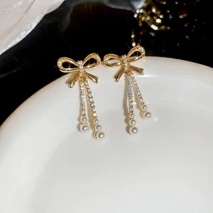 Gold bow earrings with zircon tassels and white pearls shown on a ceramic plate