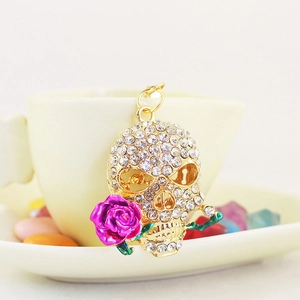 Golden skull keychain with purple rose and white crystals on a cream ceramic cup