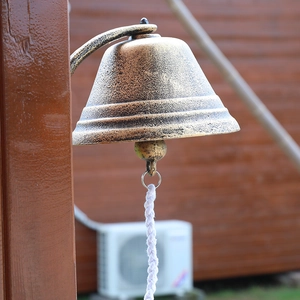 Vintage industrial style oversized cast iron wall bell with white pull rope hanging