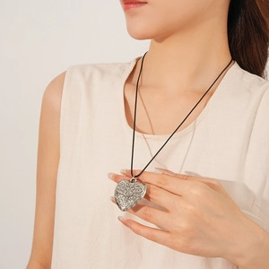 Close-up of a large silver heart pendant with floral engraving on a black cord necklace