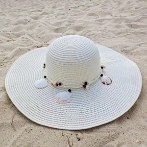 Close-up of white woven straw sun hat with shell and wood bead details on the beach