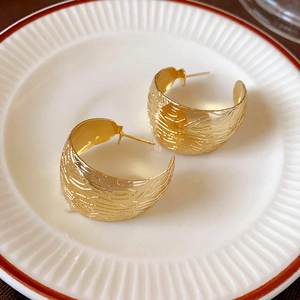 Macro shot of gold-plated wide earrings with wavy texture on a ceramic plate