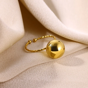 Détail de la bague boule dorée polie avec un anneau torsadé sur un tissu en satin