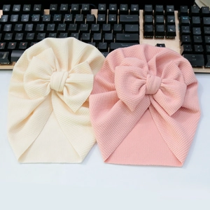 Detail of ribbed knit baby turban hats in beige and pink with large decorative bows