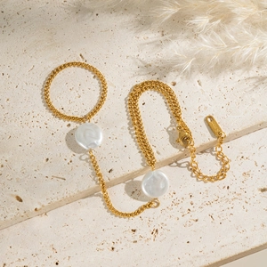 Elegant gold stainless steel pearl finger chain bracelet on a textured stone background