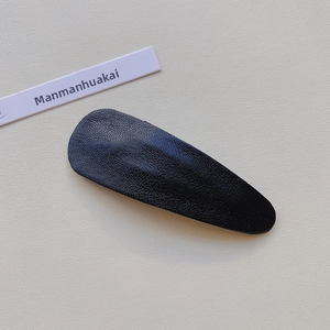Close-up of black lychee grain PU leather drop-shaped hair clip on a minimalist card