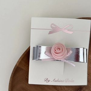Detail of silver bow hair clip with pink rose and rhinestones on a display card