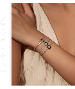 Close-up of stacked S925 silver tennis bracelets with geometric black enamel charms