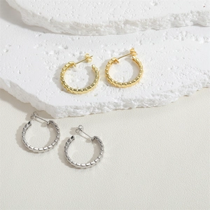 Detailed close-up of gold and silver textured hoop earrings on a white stone background