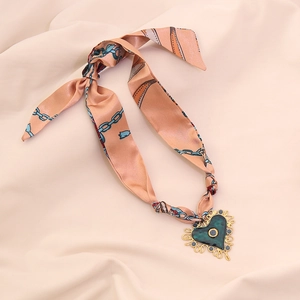 Detail view of heart pendant on peach silk scarf necklace with ornate gold border