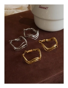 Detailed view of silver and gold irregular twisted hoop earrings on a dark surface