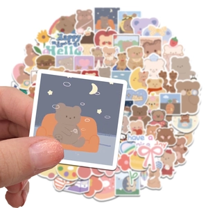 Close-up of cute cartoon bear sticker being held over a pile of colorful waterproof decals