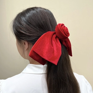 Détail d'un nœud papillon géant en velours rouge avec rose porté en queue de cheval