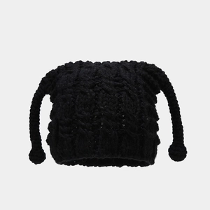 Detail of black chunky knit beanie with long braided tassels and decorative poms