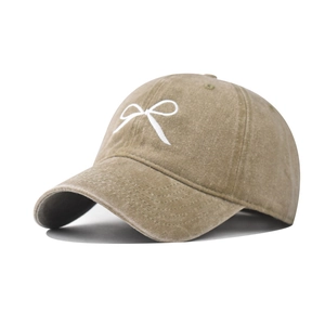 Detailed embroidery of a white bow on a washed khaki cotton baseball cap with textured finish
