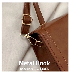Detail of high-quality gold hardware hook and strap buckle on a brown leather square bag