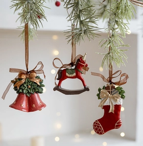 Close-up of resin Christmas ornaments featuring red bells, rocking horse, and socks on pine