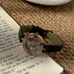 Elegant rose gold ladies watch with diamond bezel and black quilted strap on a book