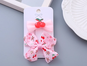 Detail of pink bow hair clips with cherry motifs set on a white card for girls