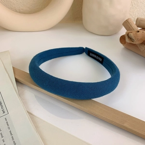 Detail showing blue padded wide headband with a black handmade woven label on white surface