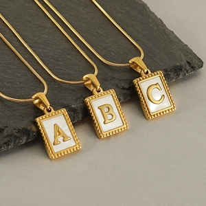 Detailed view of gold snake chains with rectangular mother of pearl letter pendants