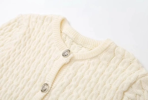Detail of cream knit cardigan featuring intricate cable texture and embossed silver buttons