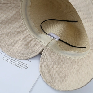 Détail d'un chapeau de soleil beige avec cordon coupe-vent et texture de bord ondulé