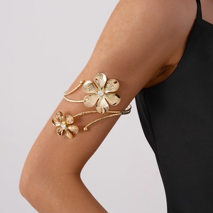 Detailed view of a golden metal arm cuff featuring crystal-set flower motifs and textured bands