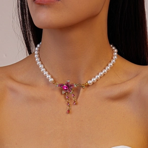 Macro detail of faux pearl necklace featuring a pink rhinestone flower and gold tassels
